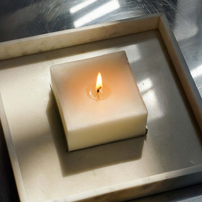 Candela profumata quadrata Effusione Eterna 1 accesa su superficie in marmo