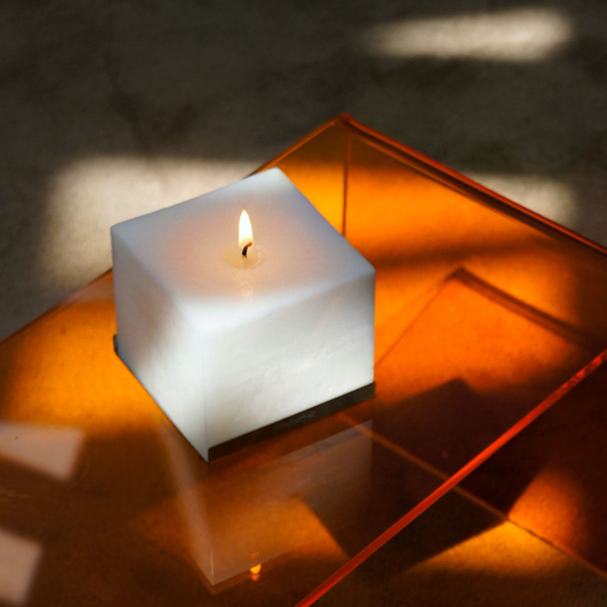 Candela profumata Effusione Eterna 2 accesa su superficie in vetro dal design elegante