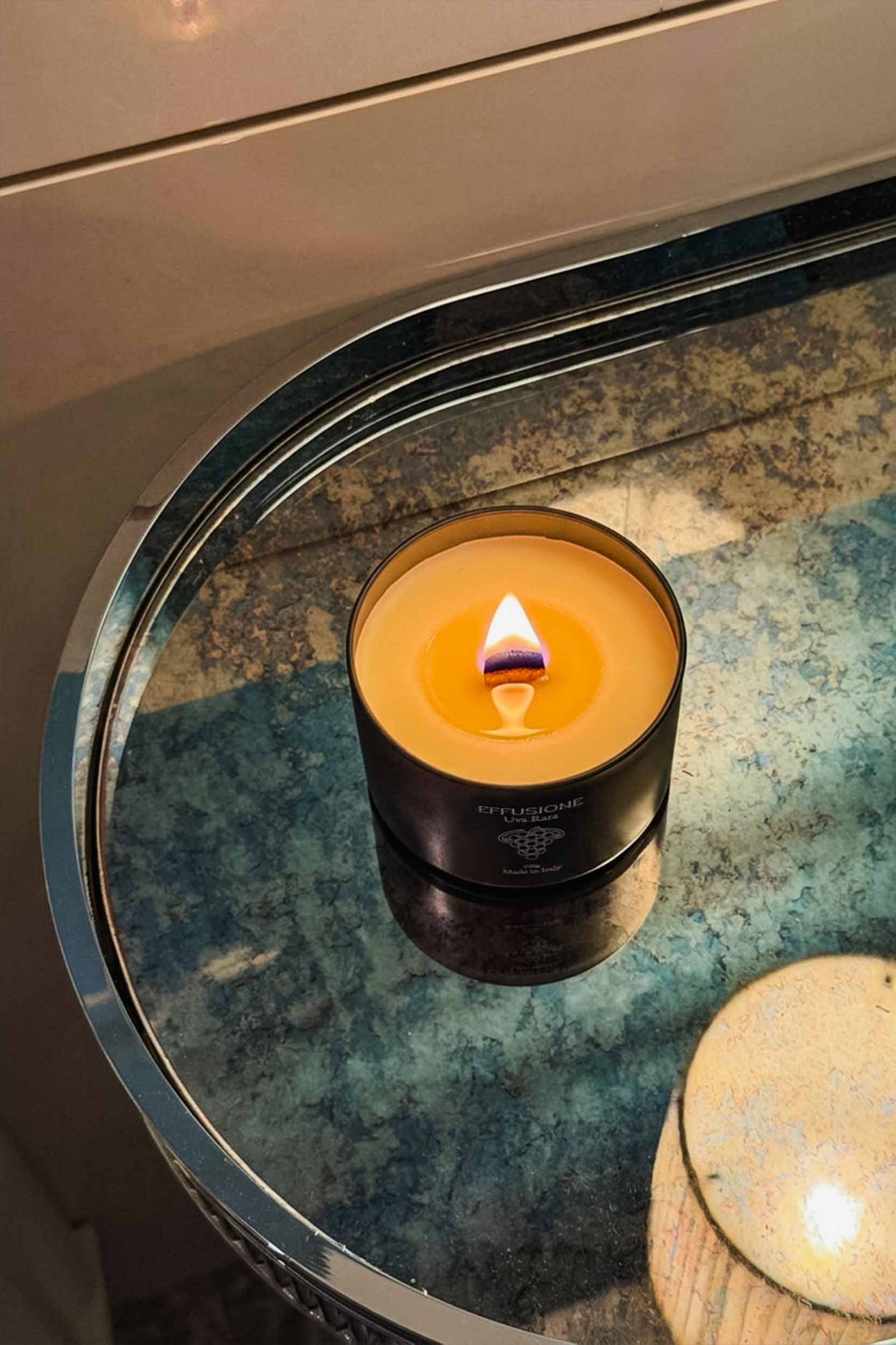 Candela profumata Echo Effusione fragranza Uva Rara accesa su tavolo di design