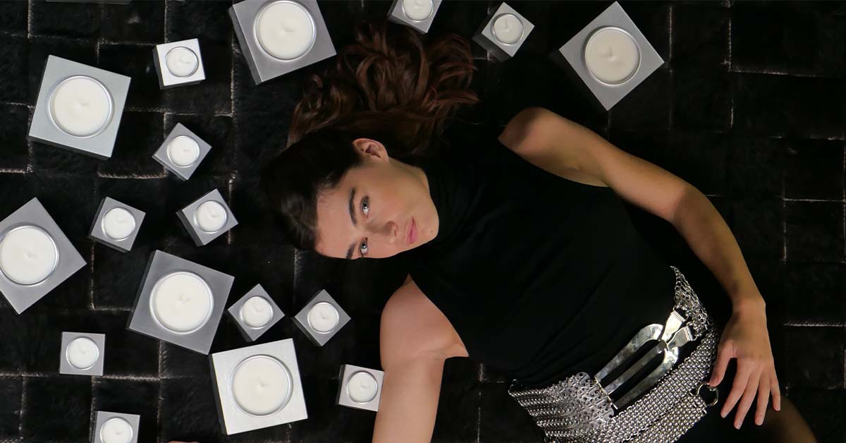 Modella in posa circondata da candele magnetiche Aura in alluminio satinato, foto lifestyle a tema design.